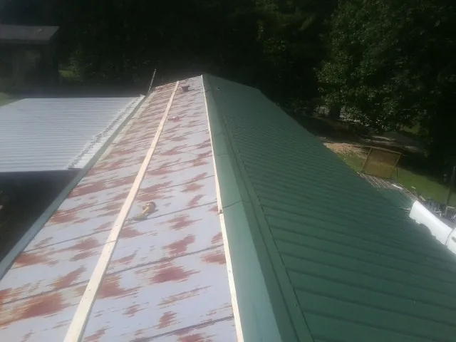 Old rusted panels beside newly installed green metal roofing — Wind Damage Roof Repair by Roofing Brothers in Flintstone