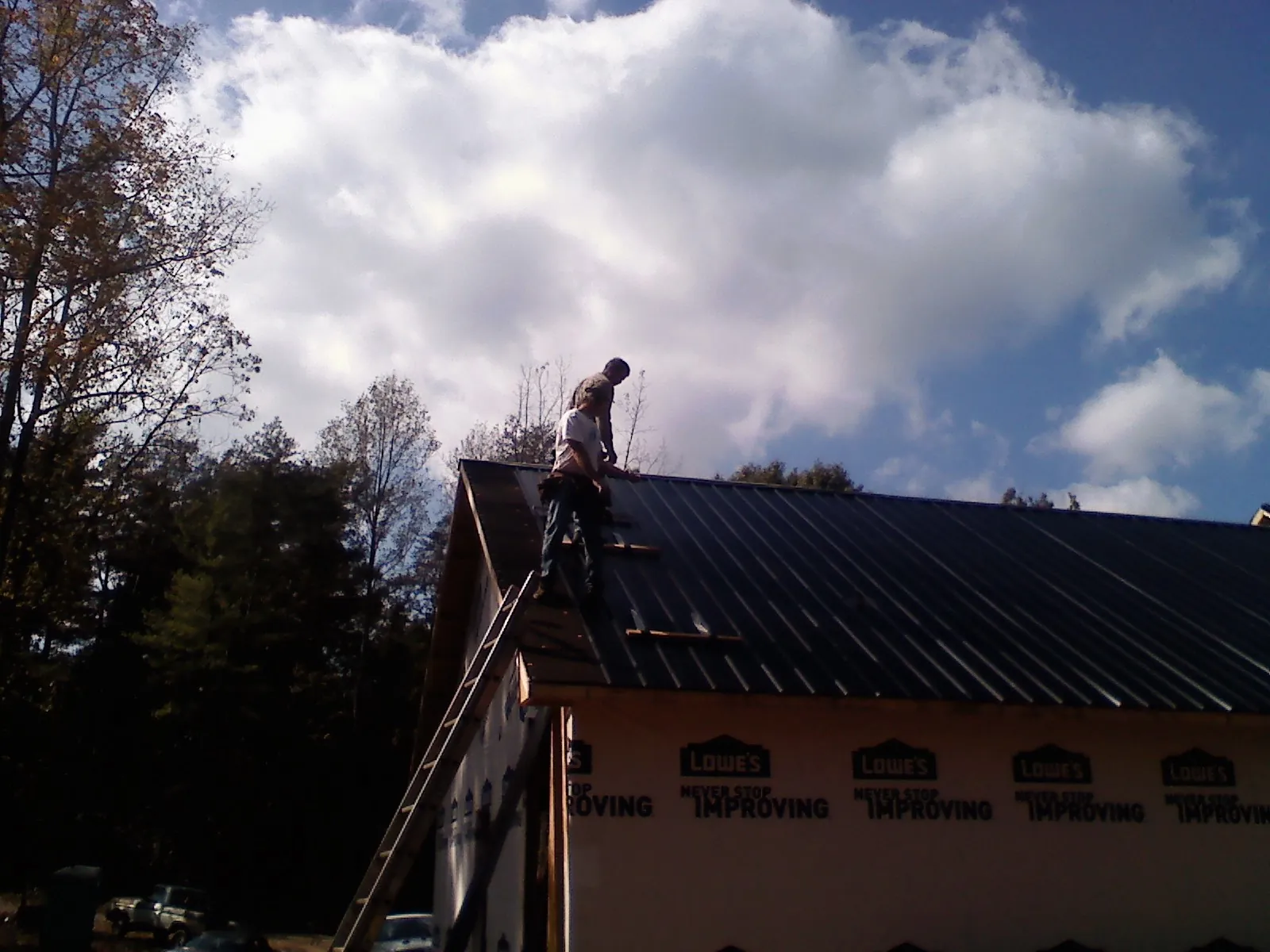 Roofer fastening dark metal panels high against a cloudy sky, from a Roof Inspection job in Flintstone